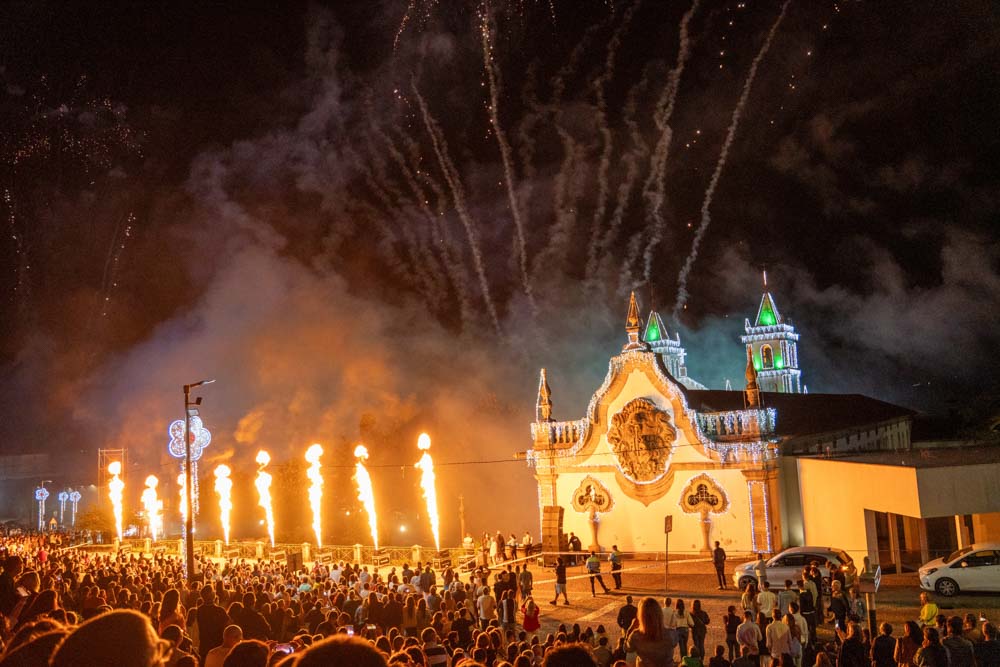 Eine große Menschenmenge beobachtet das lebhafte Fest São Bento 2025 in Santo Tirso, bei dem Feuerwerk und Feuersäulen die kunstvolle Kirchenarchitektur erleuchten. Alle anwesenden Delegationen sind von der festlichen Szene begeistert.