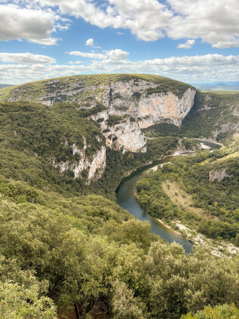 Ein gewundener Fluss fließt durch ein üppiges, grünes Tal in der Nähe von Saint-Péray, umgeben von steilen Felsen und bewaldeten Hügeln unter einem teilweise bewölkten Himmel - eine idyllische Kulisse für das Wein- und Verschwisterungsfest 2025.